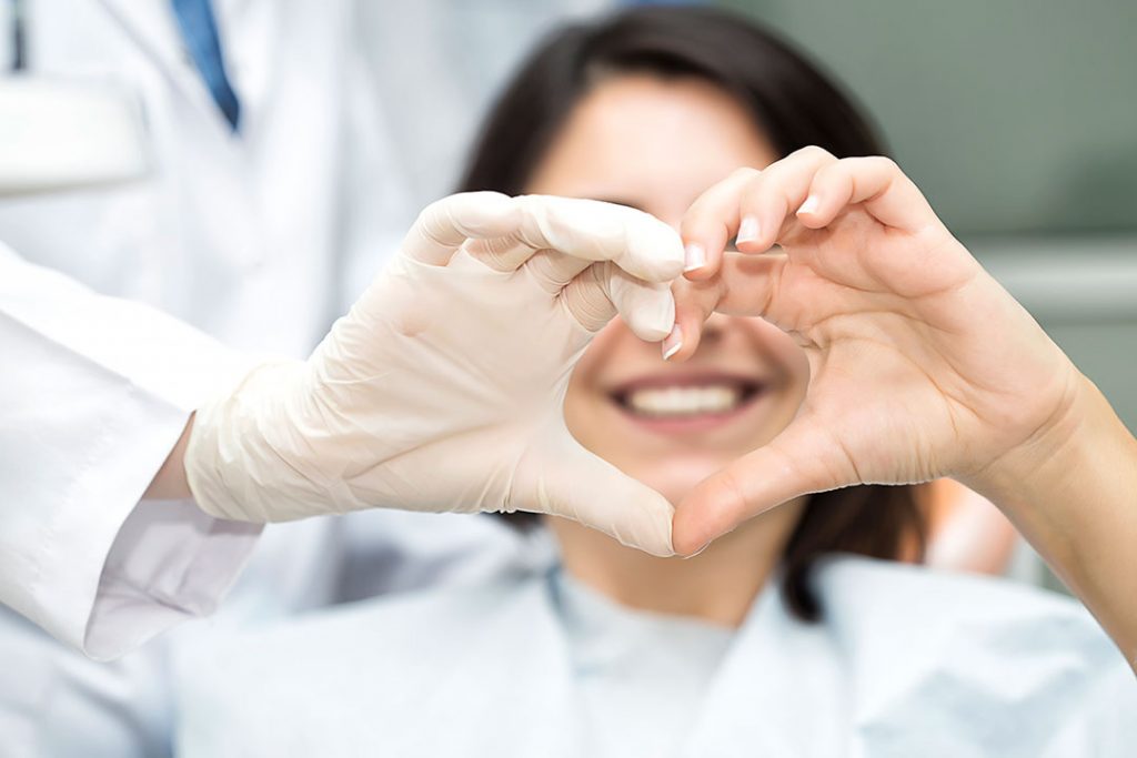Male dentist and female patient making a heart with their hands
